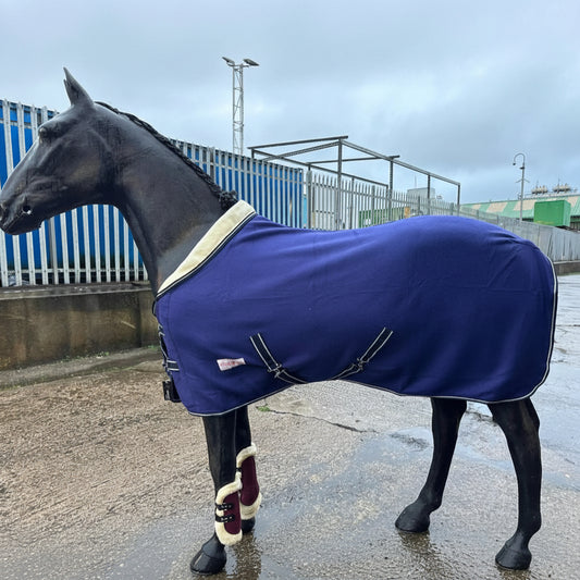 A horse wearing a blue personalized show fleece with a fur collar cooler, standing outdoors.