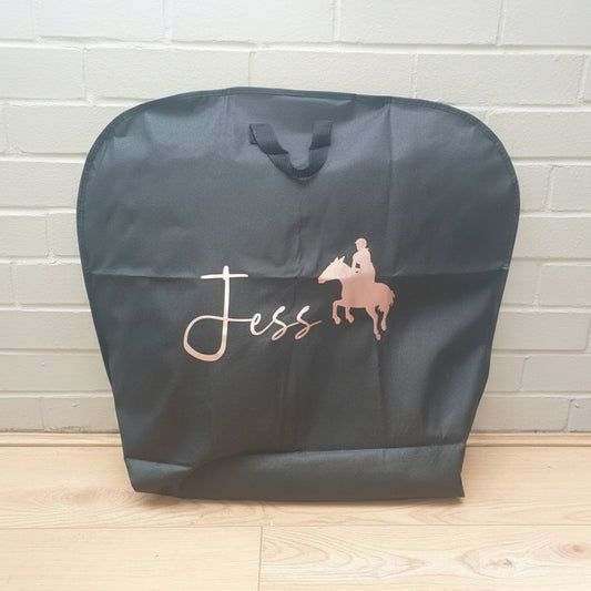 A black personalised equestrian saddle pad bag with the name 'Jess' printed in pink. The bag has a handle and is placed against a grey background.